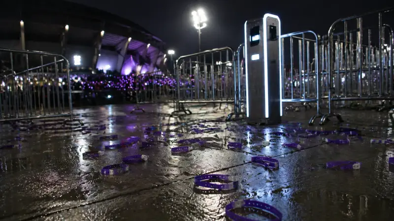 BTS wristband theft scene at a rain-soaked stadium gate with purple bands scattered on the ground